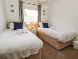 Two single beds in a bedroom with curtains and a lamp at Tides Corner Bowleaze