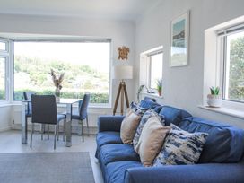 A sitting room with a blue sofa and dining table with grey chairs near large windows at 2 Rockmount in Salcombe