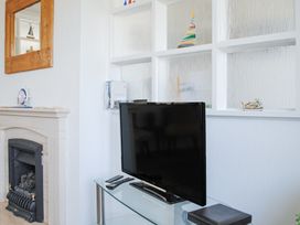A corner of a living room with a television on a glass stand next to a fireplace and a wooden framed mirror at 2 Rockmount in Salcombe