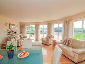 A living room with beige leather sofas and large windows overlooking a green landscape at 2 Sea Gardens in Hope Cove