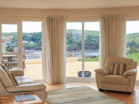 A living room with beige leather sofas and large windows overlooking a patio and green hills at 2 Sea Gardens in Hope Cove