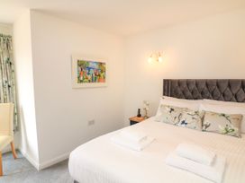 A bedroom with a bed with pillows and towels a bedside table with a lamp and phone a chair and a painting on the wall at 2 Sea Gardens in Hope Cove