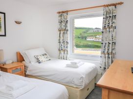 A bedroom with two single beds a wooden desk a window with curtains overlooking green hills at 2 Sea Gardens in Hope Cove