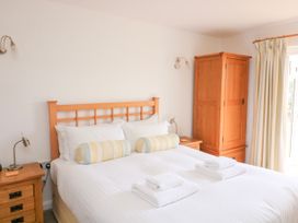 A bedroom with a double bed white bedding two striped bolster pillows wooden bedside tables and a wooden wardrobe at 2 Sea Gardens in Hope Cove