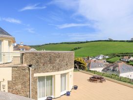 A terrace with a round wooden picnic table and stone wall overlooking green hills and houses at 2 Sea Gardens in Hope Cove