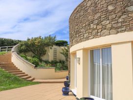 An exterior view of a stone and cream building with sliding glass doors a staircase and garden area at 2 Sea Gardens in Hope Cove
