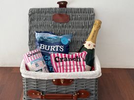 A woven picnic basket containing a bottle of champagne and packets of crisps and sweets