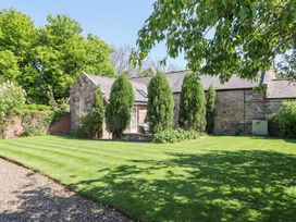 A stone cottage with a slate roof surrounded by a garden with trimmed grass and evergreen trees at The Coach House in Lowick near Holy Island