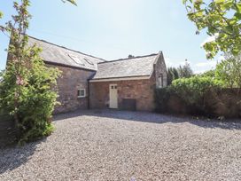 A gravel driveway in front of a stone building with a sloped roof and white door surrounded by bushes at The Coach House in Lowick near Holy Island