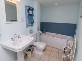 A bathroom with a sink, toilet, bathtub, blue wall shelf, and towel rack at The Coach House in Lowick near Holy Island