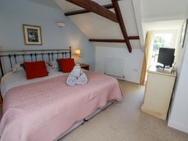 A bedroom with a double bed, red cushions, rolled towels, a bedside table with a lamp, a chest of drawers with a TV, and exposed wooden beams at The Coach House in Lowick near Holy Island