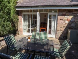 An outdoor patio with a glass table and six checked cushioned chairs outside a stone building with white framed French doors at The Coach House in Lowick near Holy Island
