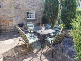 A patio with a metal table and six cushioned chairs with a bottle and two glasses on the table at The Coach House in Lowick near Holy Island
