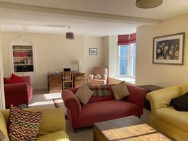 A living room with red and yellow sofas a wooden desk and chair a built in bookshelf and a window with red blinds at Sant Seiriol in Beaumaris