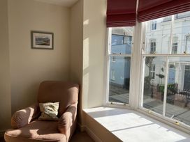 A corner with an armchair and pillow next to a bay window with red blinds and a framed picture on the wall at Sant Seiriol in Beaumaris