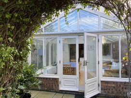 A glass conservatory with white framed doors and windows showing wooden table and chairs inside at Sant Seiriol in Beaumaris