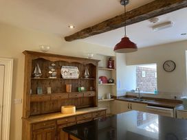A kitchen with wooden cabinets a black countertop a wooden hutch with decorations and shelves a red pendant light and a clock on the wall at Sant Seiriol in Beaumaris