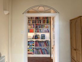 A room with a white framed doorway leading to a bookcase filled with books and board games and a wooden wardrobe to the right at Sant Seiriol in Beaumaris