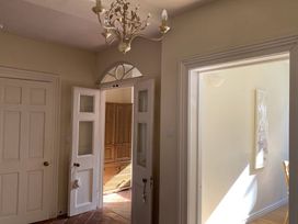 A hallway with open white doors leading to a room with wooden furniture and sunlight coming through at Sant Seiriol in Beaumaris