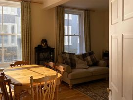 A dining table with wooden chairs and a sofa with cushions in a room with two windows at Sant Seiriol in Beaumaris