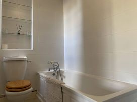 A bathroom with a toilet with wooden seat and a bathtub with a towel at Sant Seiriol in Beaumaris