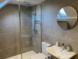 A bathroom with a shower area a toilet a sink a round mirror and a skylight at Sant Seiriol in Beaumaris
