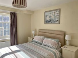 A bedroom with a bed with striped bedding bedside tables with lamps a window with curtains and a painting of sailboats on the wall at Sant Seiriol in Beaumaris