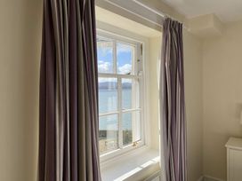 A window with striped curtains overlooking a body of water and hills at Sant Seiriol in Beaumaris