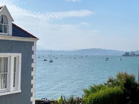 A view of a body of water with multiple sailboats and a grey house on the left side at Sant Seiriol in Beaumaris
