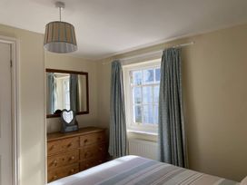 A bedroom with a wooden dresser with mirror and a heart-shaped vanity mirror next to a window with polka dot curtains at Sant Seiriol in Beaumaris
