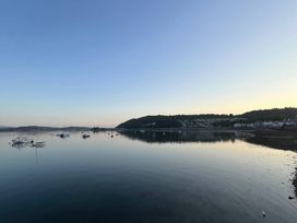 A calm body of water with boats anchored and houses on a hillside at Sant Seiriol in Beaumaris