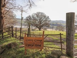 A wooden sign with Conwy Cottage Cymryd Uchaf near a fence and a field with trees and hills in the background at Cymryd Uchaf in Conwy