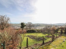 A garden with grass and leafless bushes overlooking hills and a body of water at Cymryd Uchaf in Conwy