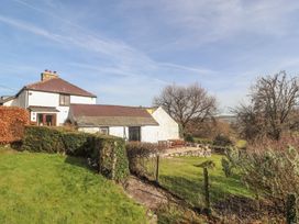 A grassy garden with bushes a stone patio and a white stone house with a tiled roof at Cymryd Uchaf in Conwy