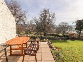 A wooden table and bench on a patio overlooking a grassy yard with trees and a stone wall at Cymryd Uchaf in Conwy