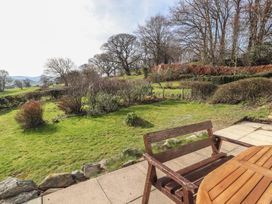 A garden with grass bushes and trees viewed from a patio with a wooden bench and table at Cymryd Uchaf in Conwy