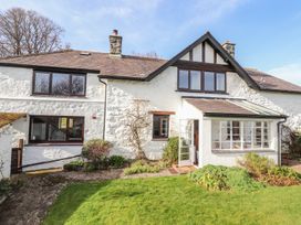 A white stone house with dark framed windows and a glass porch surrounded by a garden at Cymryd Uchaf in Conwy