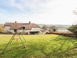 A grassy yard with a swing set and a white house with a tiled roof in the background with hills behind at Cymryd Uchaf in Conwy