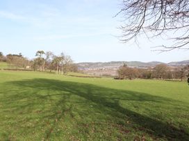 A grassy field with trees and hills in the distance at Cymryd Uchaf in Conwy