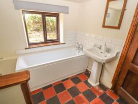 A bathroom with a bathtub under a window and a pedestal sink with a mirror above at Cymryd Uchaf Conwy