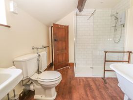 A bathroom with a toilet a wooden door a glass shower enclosure a wooden towel rack and a white sink at Cymryd Uchaf in Conwy