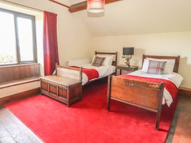 A bedroom with two wooden single beds a wooden chest a nightstand with a lamp and red carpets at Cymryd Uchaf in Conwy