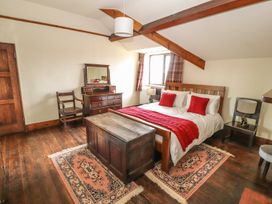 A bedroom with a double bed with white and red bedding wooden furniture and two rugs on a wooden floor at Cymryd Uchaf in Conwy