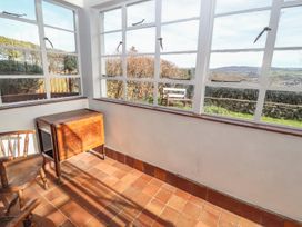 A small sunroom with terracotta floor tiles wooden chairs and a foldable wooden table at Cymryd Uchaf in Conwy