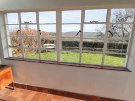 A room with tiled floor and small wooden table next to a window showing garden and hills outside at Cymryd Uchaf in Conwy