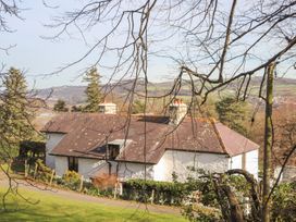 A white house with a brown roof surrounded by trees and a fence in a rural area at Cymryd Uchaf in Conwy