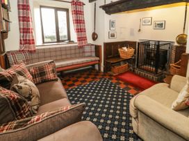 A sitting room with sofas cushions a fireplace and a window with red plaid curtains at Cymryd Uchaf in Conwy