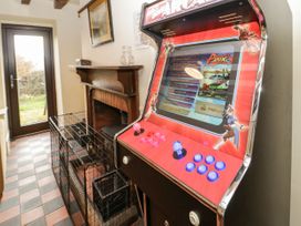 A room with a red arcade game machine next to a wooden fireplace and a wire pet crate at Cymryd Uchaf Conwy
