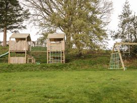 An outdoor playground with wooden climbing structures slides and swings in a grassy area at Cymryd Uchaf in Conwy