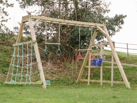 A wooden outdoor playset with swings rings climbing nets and a bucket seat in a grassy yard at Cymryd Uchaf in Conwy